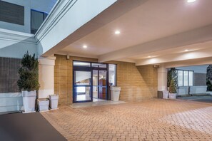 A hotel entrance with a paved driveway, a glass door entrance, and a modern building facade.