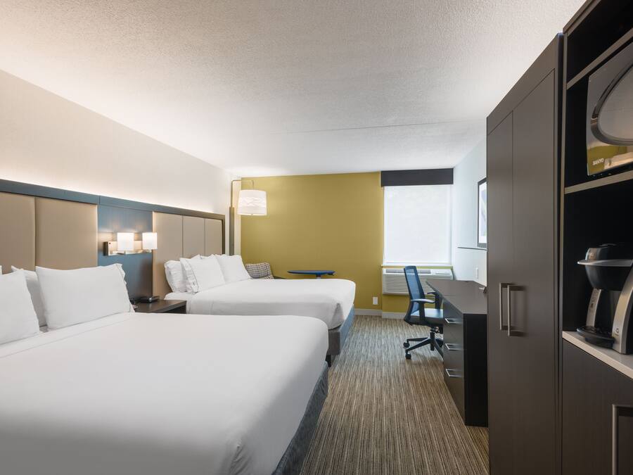 A hotel room with two beds, a desk, a chair, and a minibar.