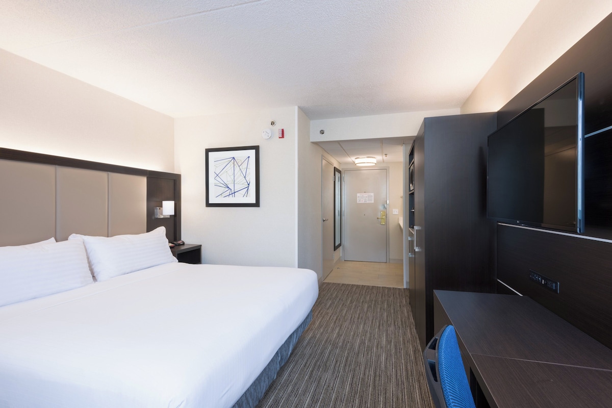 A hotel room with a bed, a desk, a TV, and a door leading to a hallway.