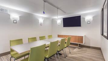 A conference room with a long table, green chairs, a whiteboard, and wall-mounted lights.