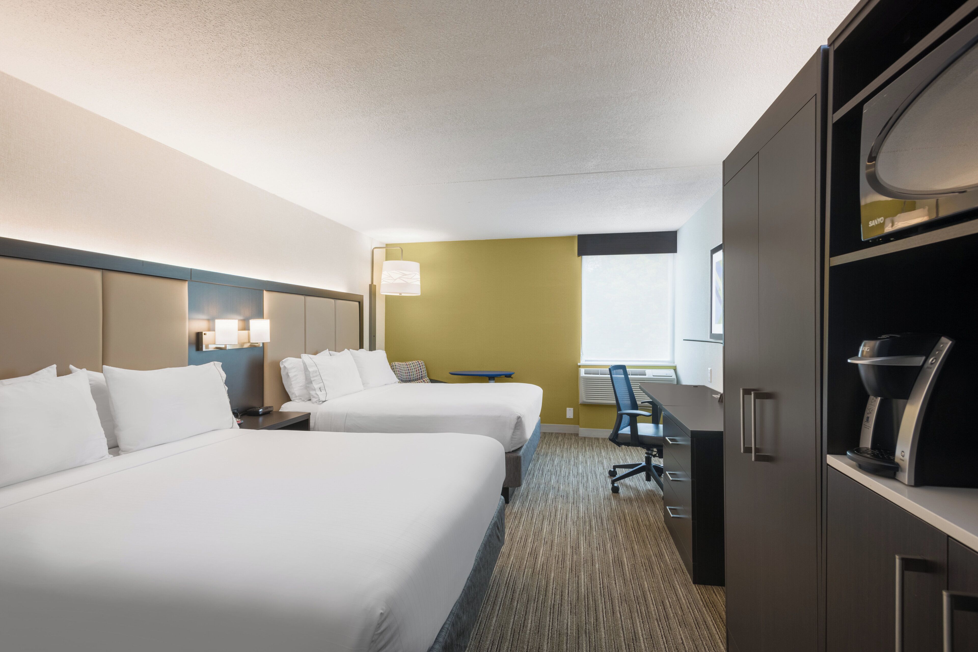 Une chambre d’hôtel avec deux lits, un bureau, une chaise, un minibar et une fenêtre.