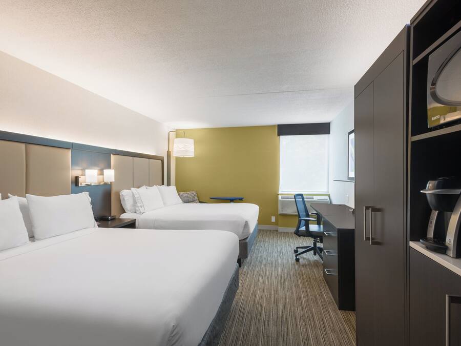 A hotel room with two beds, a desk, a chair, a minibar, and a window.