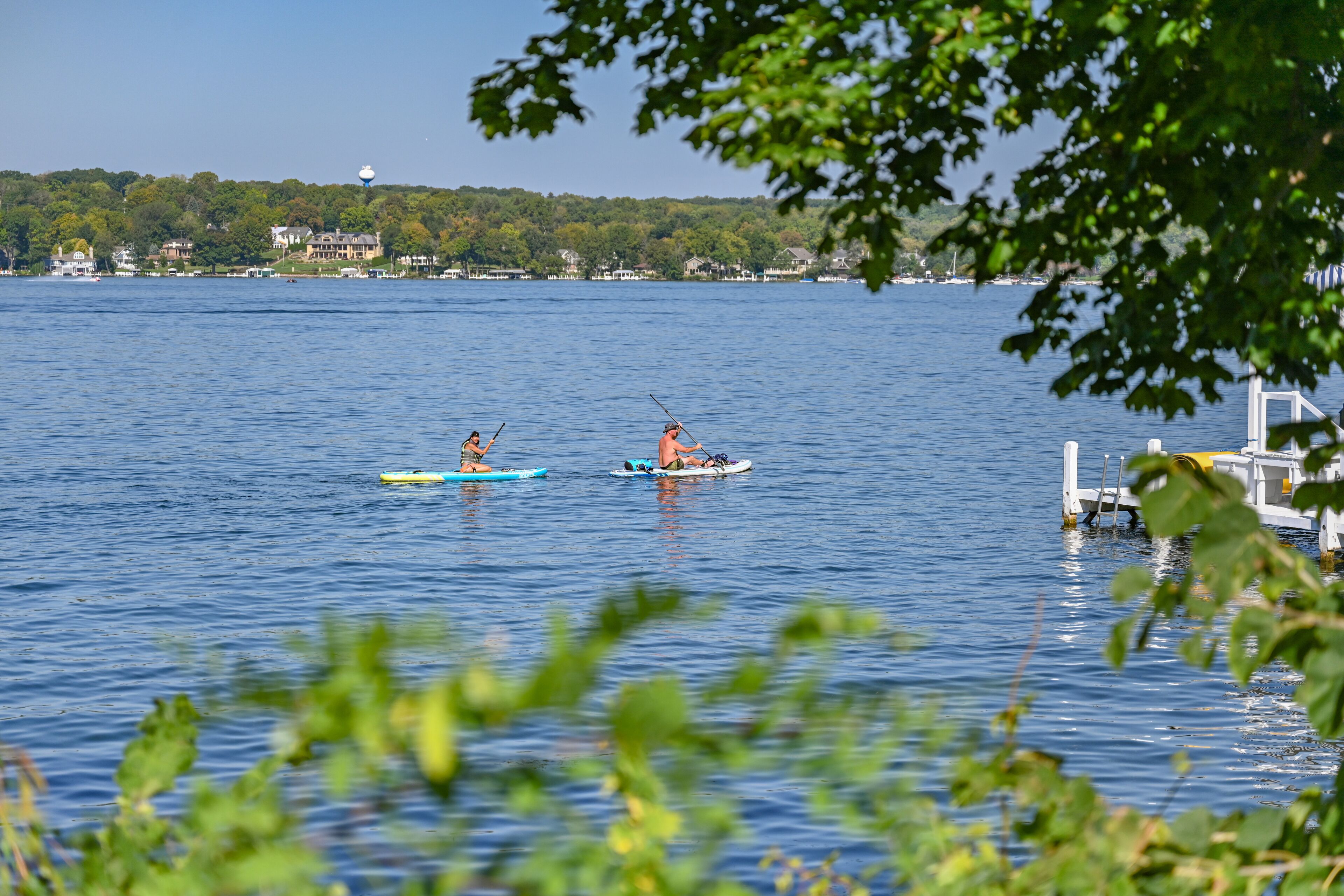 Two kayaks on a calm lake with a dock and houses in the background.