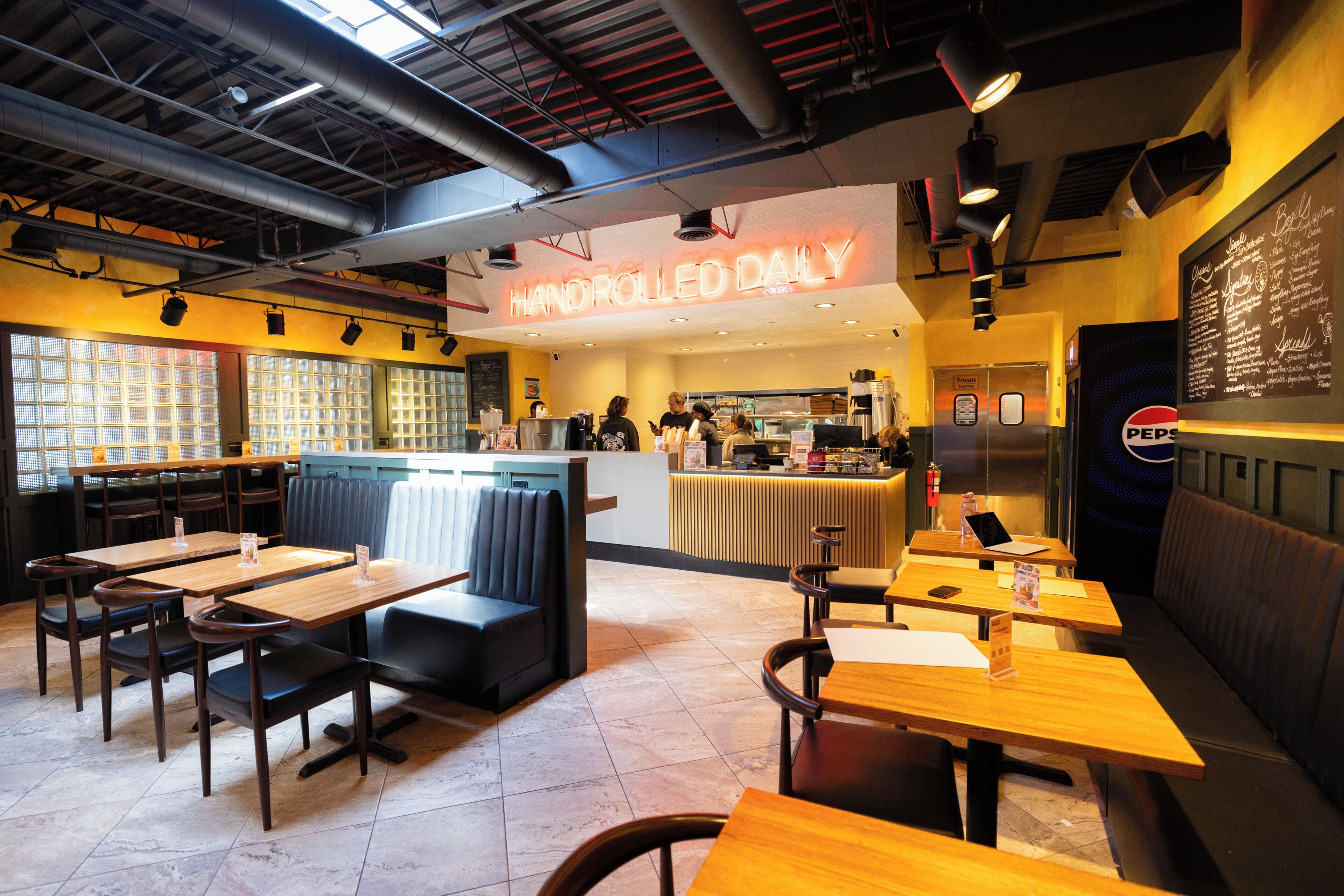 A restaurant interior with booths, tables, a neon sign, and a chalkboard menu.