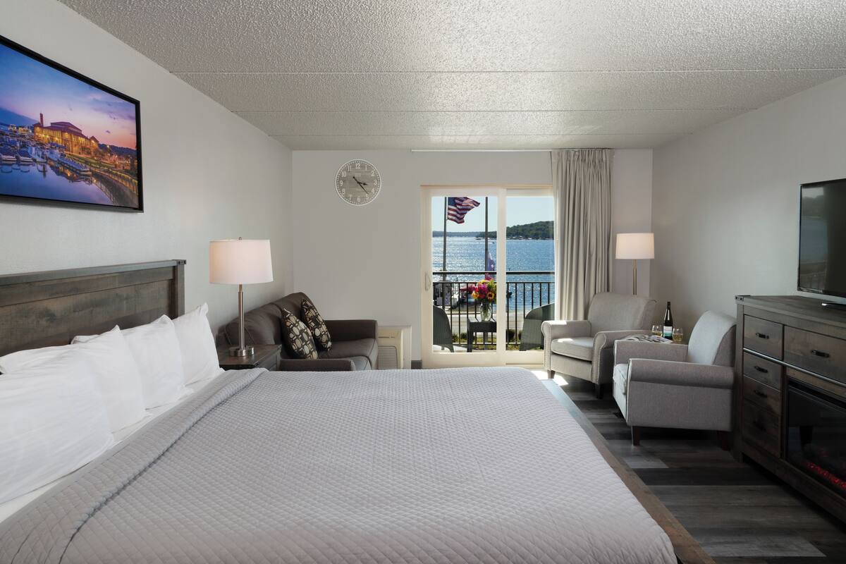 Une chambre d’hôtel avec un grand lit, une télévision, un bureau avec une lampe, une chaise et un balcon donnant sur l’eau.