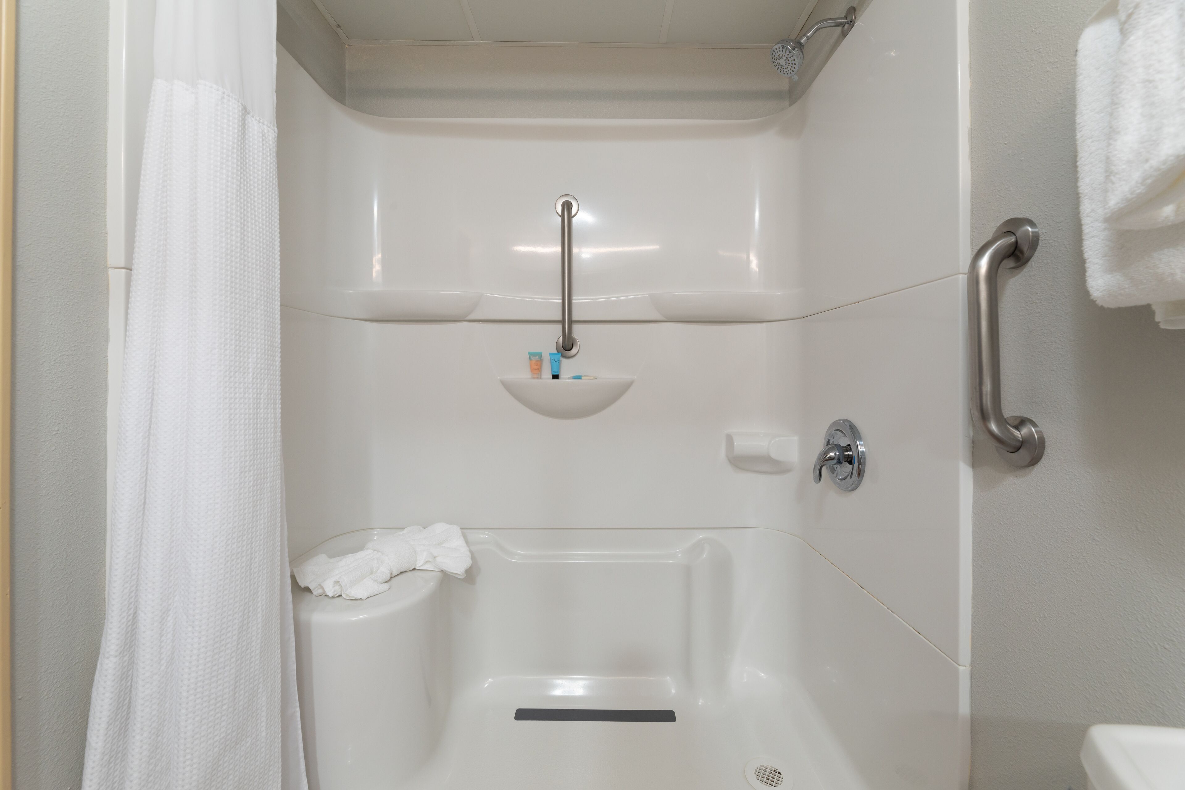Ein Badezimmer mit einer weißen Badewanne, einer Handstange, einem Handtuchhalter und einem kleinen Ablagefach für Pflegeprodukte.