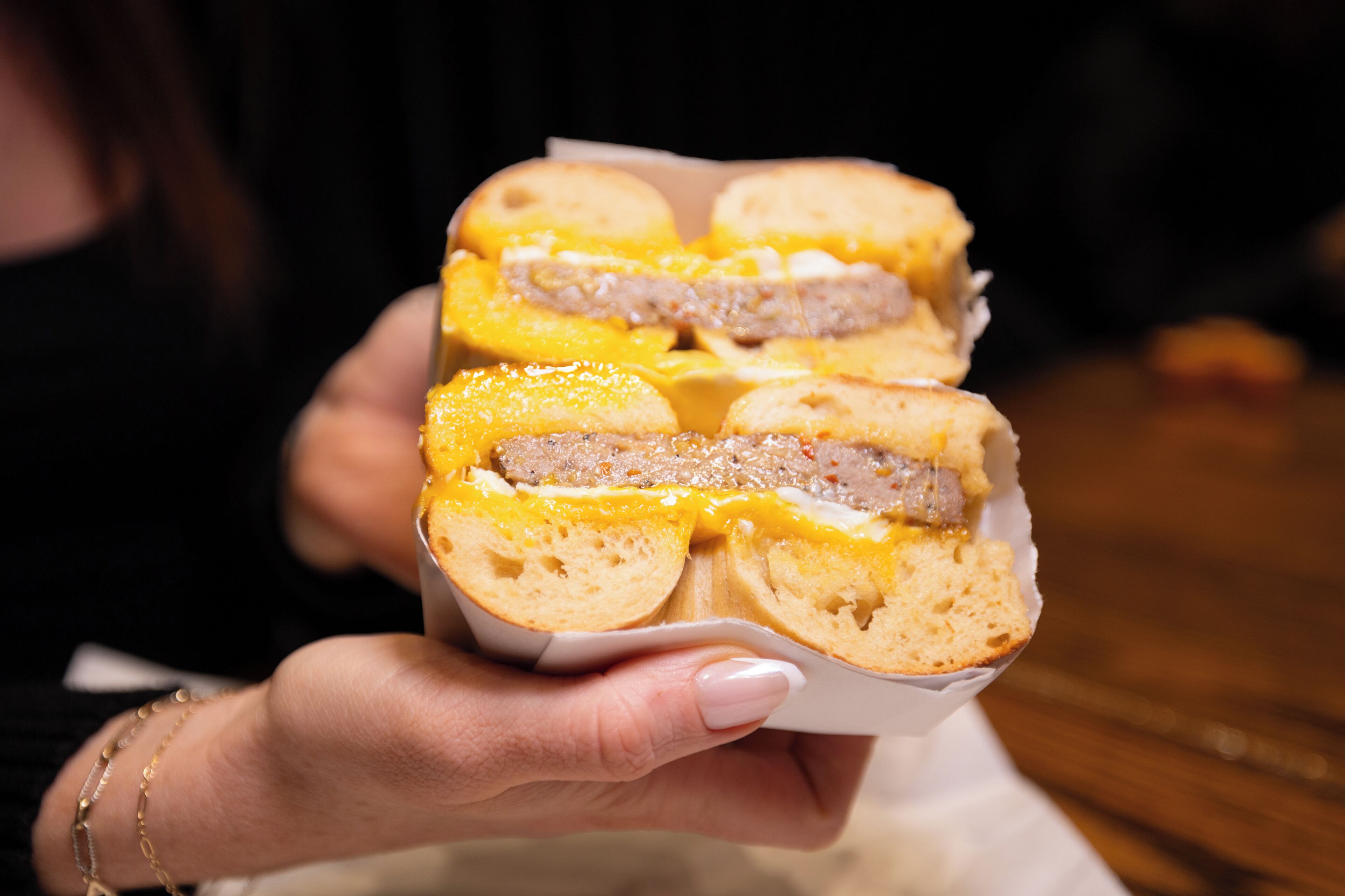 A person holding a sandwich with visible layers of meat and cheese.