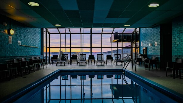 Une piscine intérieure avec de grandes fenêtres offrant une vue sur le coucher de soleil, entourée de chaises longues.