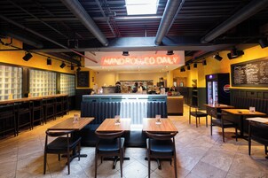 Interior de un restaurante con un letrero de neón, cabinas, mesas y una pizarra de menú.