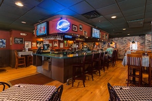 A restaurant with a bar area, wooden flooring, and checkered tablecloths.