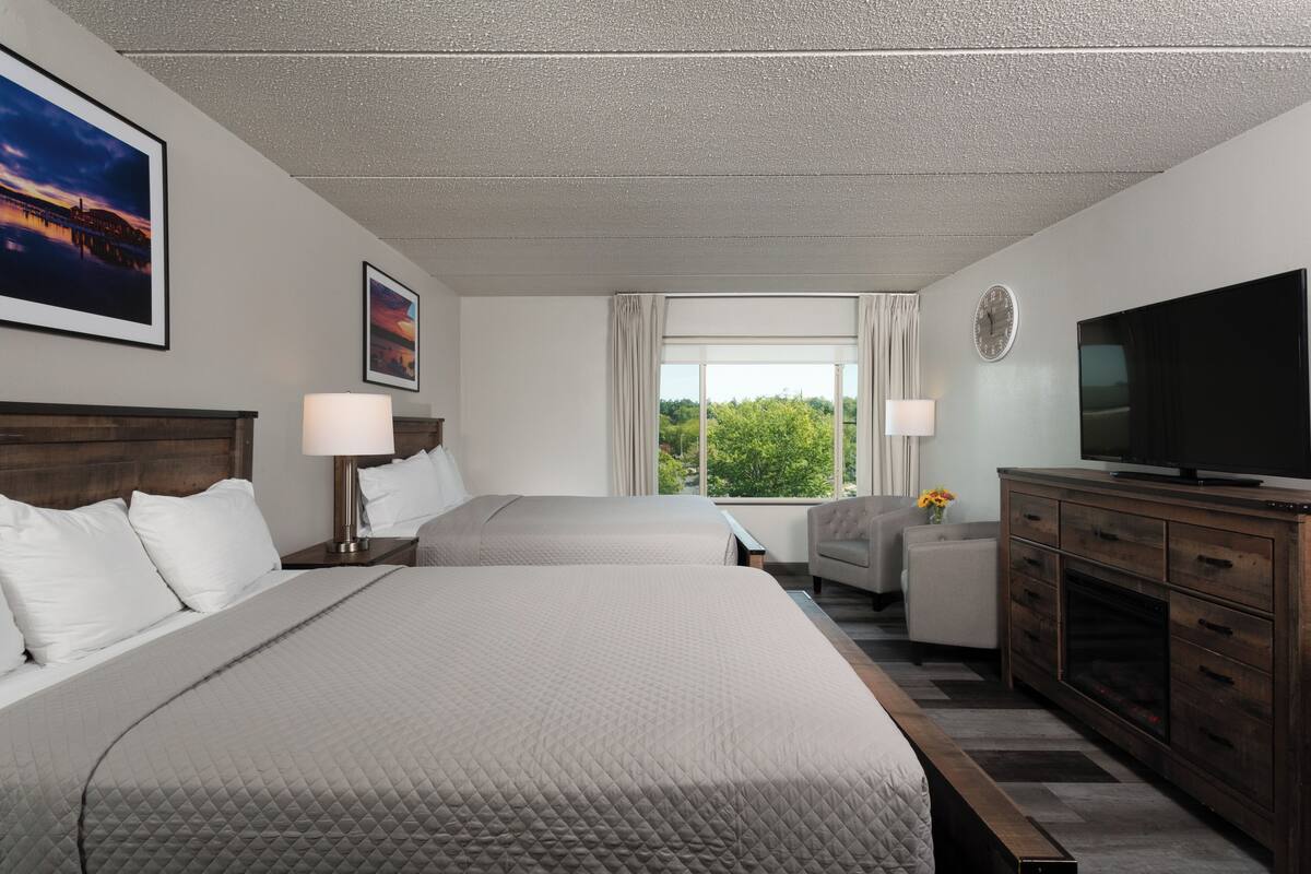 Une chambre d’hôtel avec deux lits, une télévision, un bureau et une fenêtre donnant sur un paysage verdoyant.