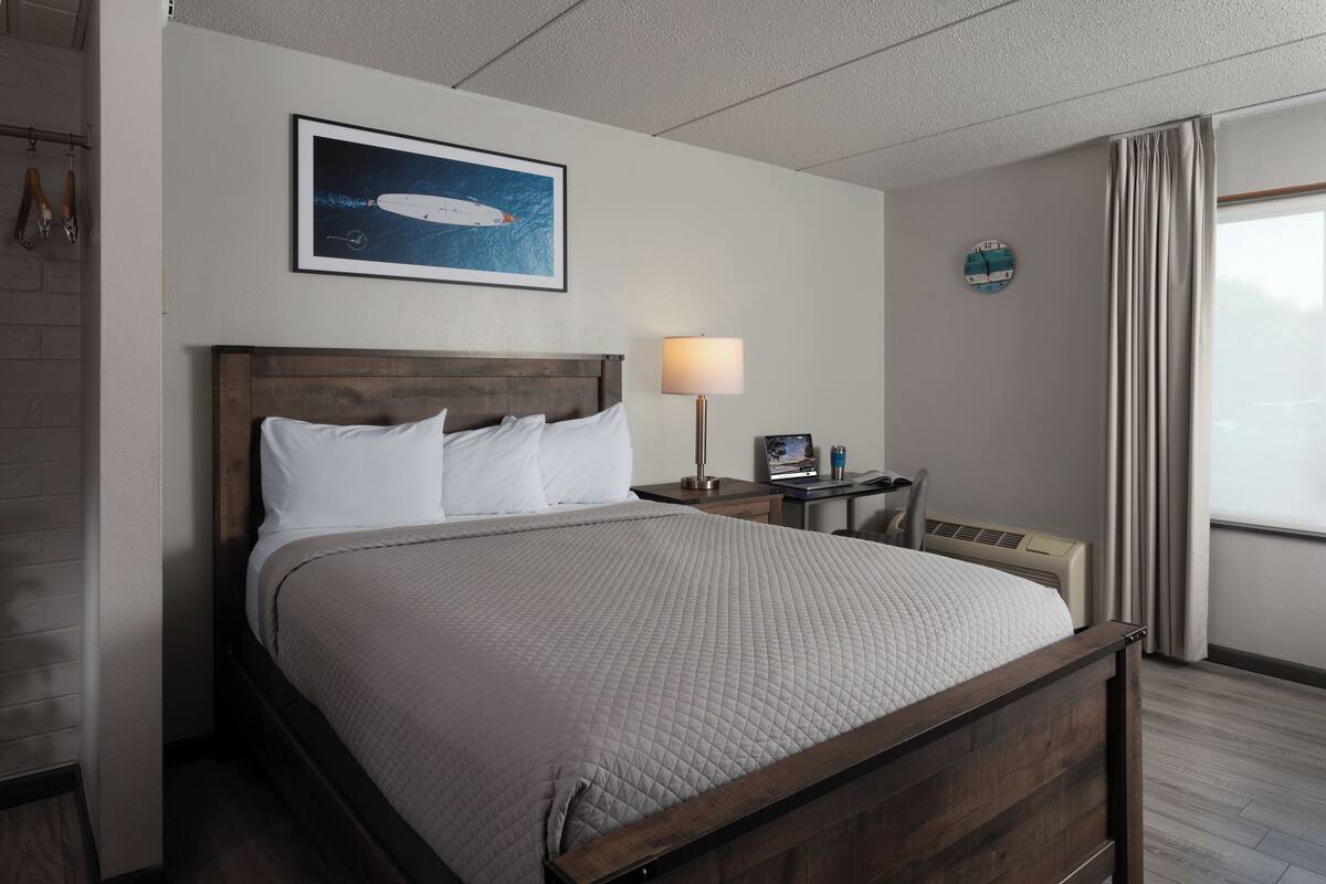 Une chambre d’hôtel avec un lit, un bureau doté d’une lampe, une horloge et une fenêtre avec des rideaux.