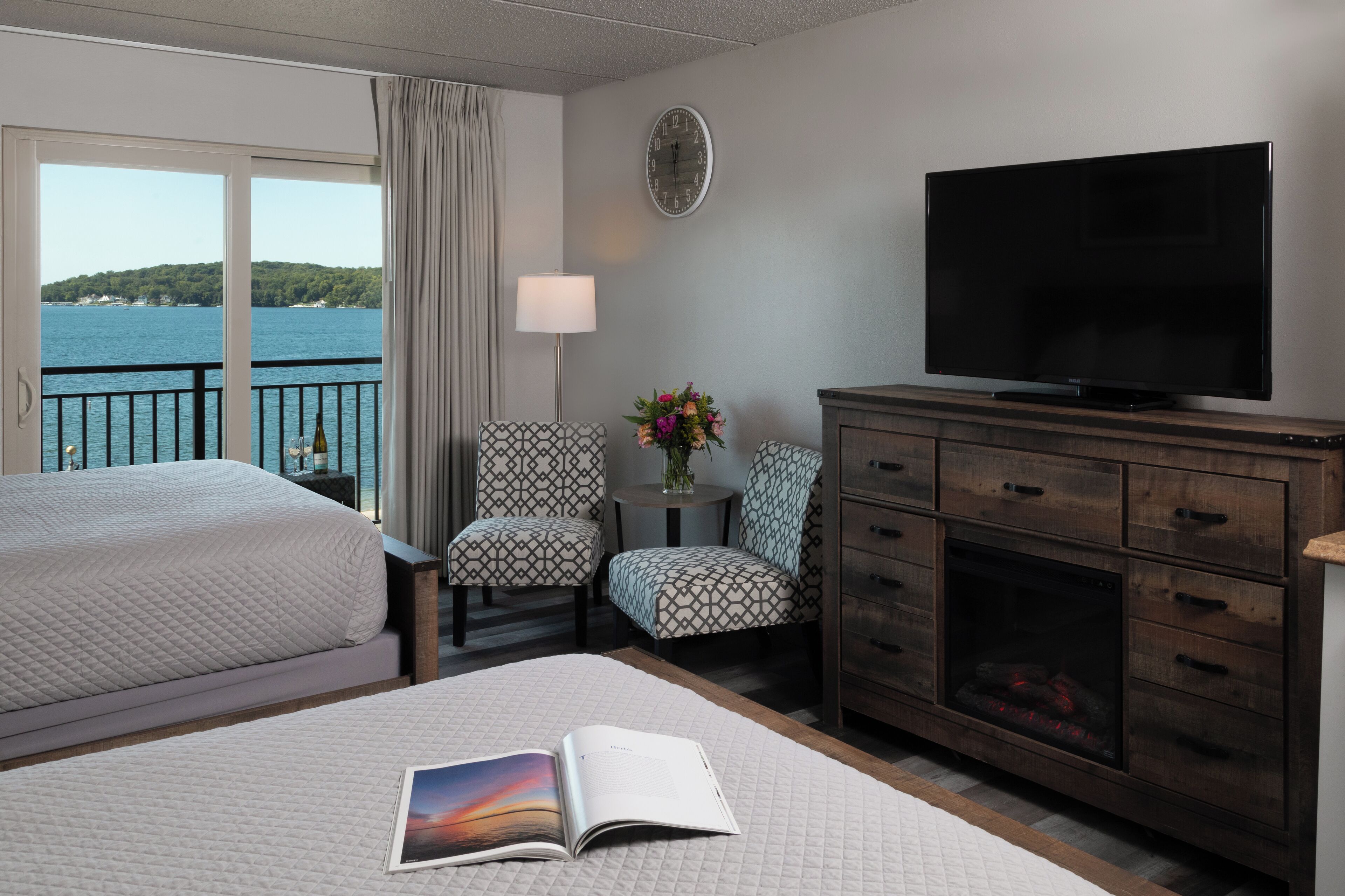 Ein Hotelzimmer mit zwei Betten, einem Fernseher, einem Kamin, einer Uhr und Meerblick.