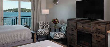 A hotel room with two beds, a TV, a fireplace, a clock, and a view of the sea.