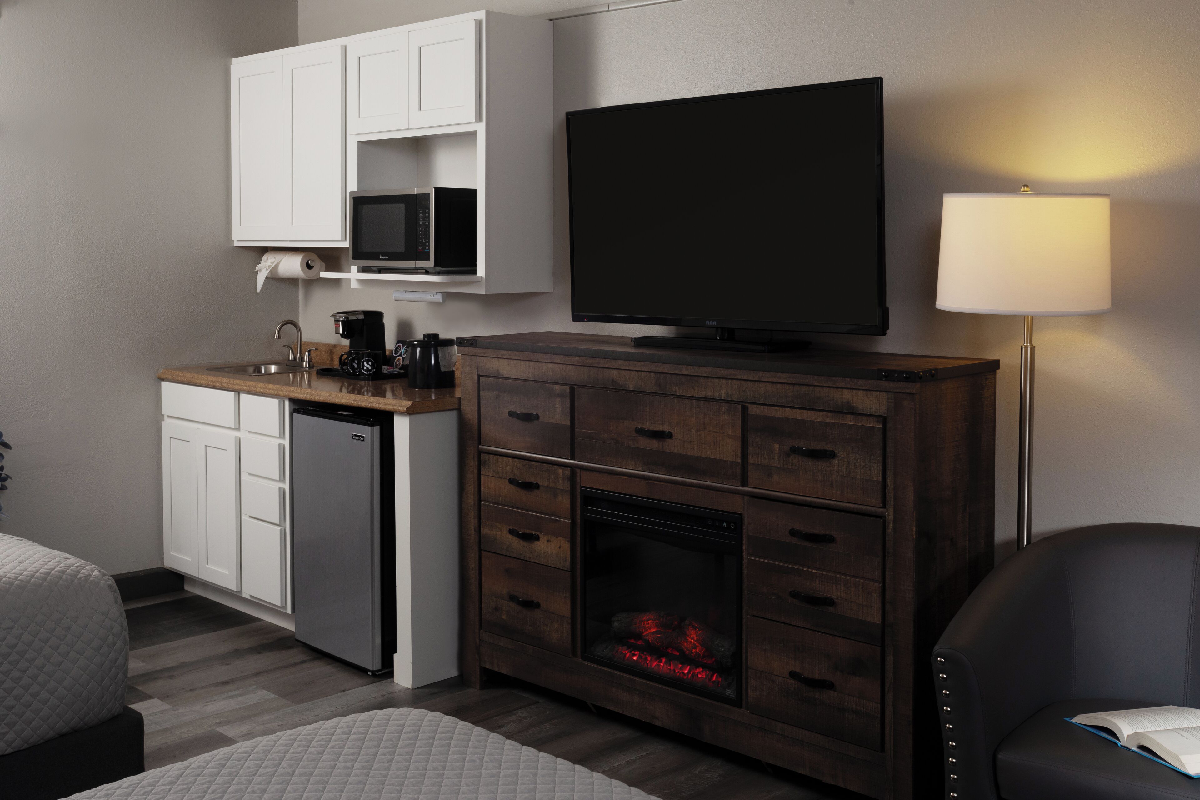 Habitación de hotel con kitchenette, televisión de pantalla plana, chimenea, lámpara y cama.