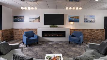 Un espacio lounge moderno con chimenea, dos sillones azules, un sofá gris y una mesa de centro con revistas.