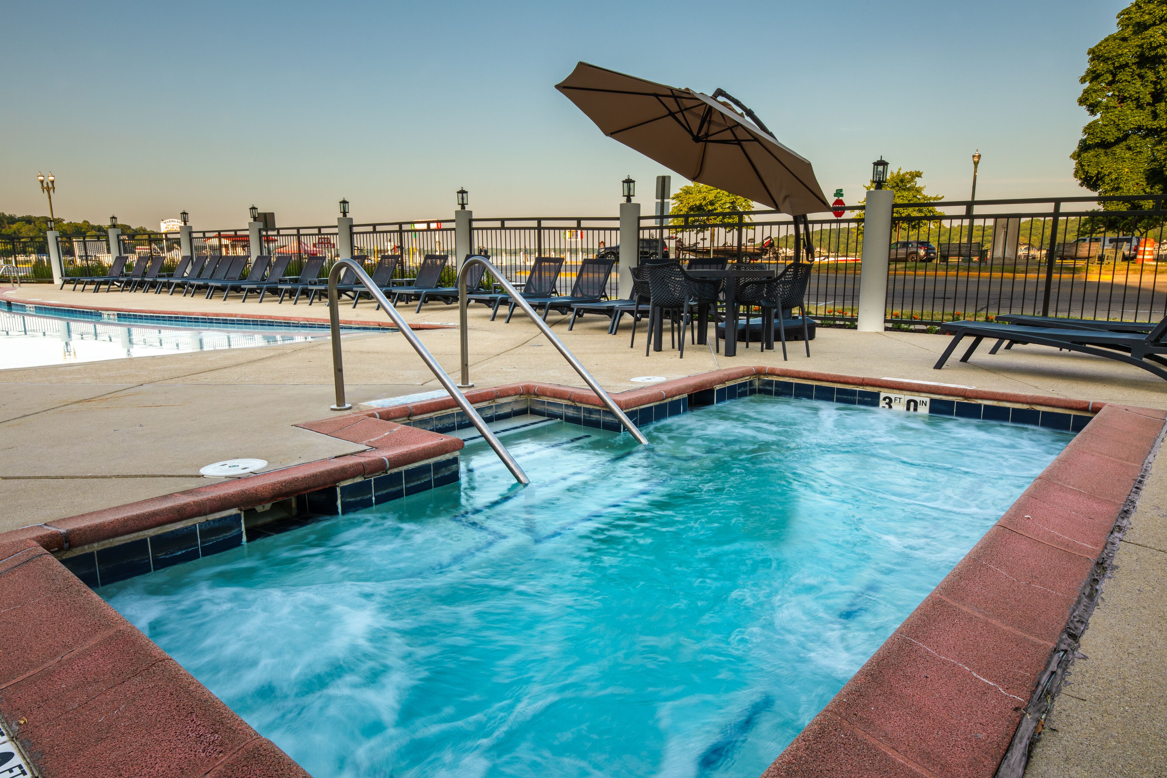 A swimming pool with a tiled edge, lounge chairs, and a table with umbrellas.