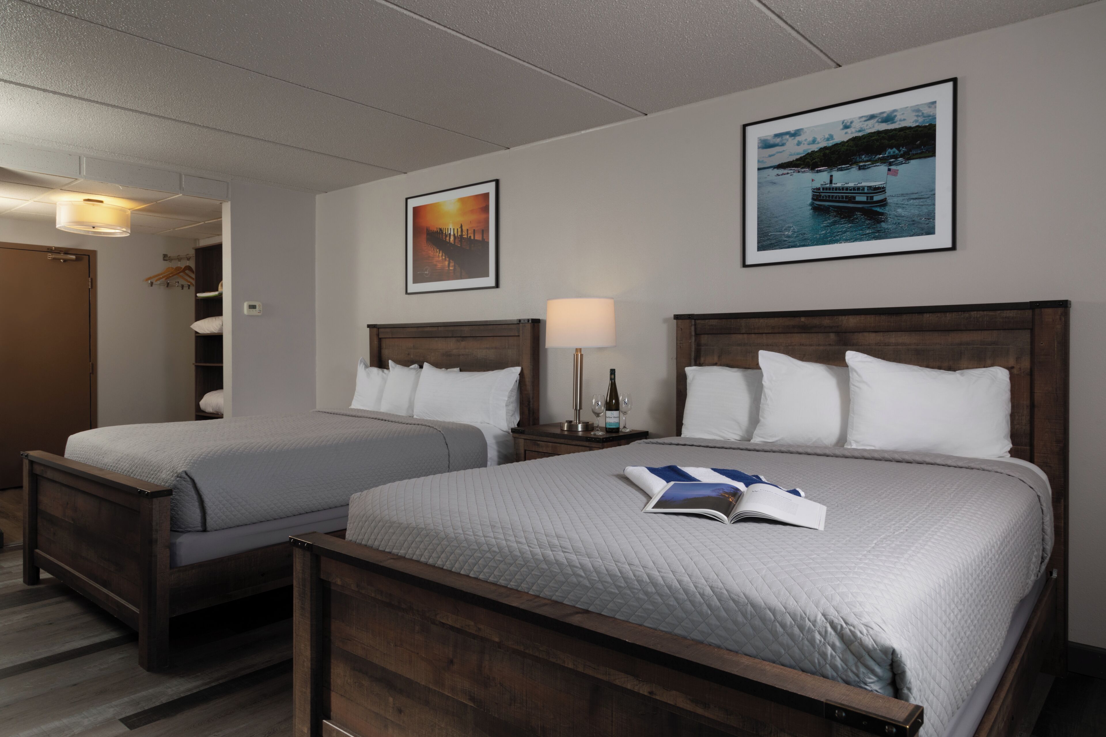 A hotel room with two beds, a nightstand with a lamp, and two framed pictures on the wall.