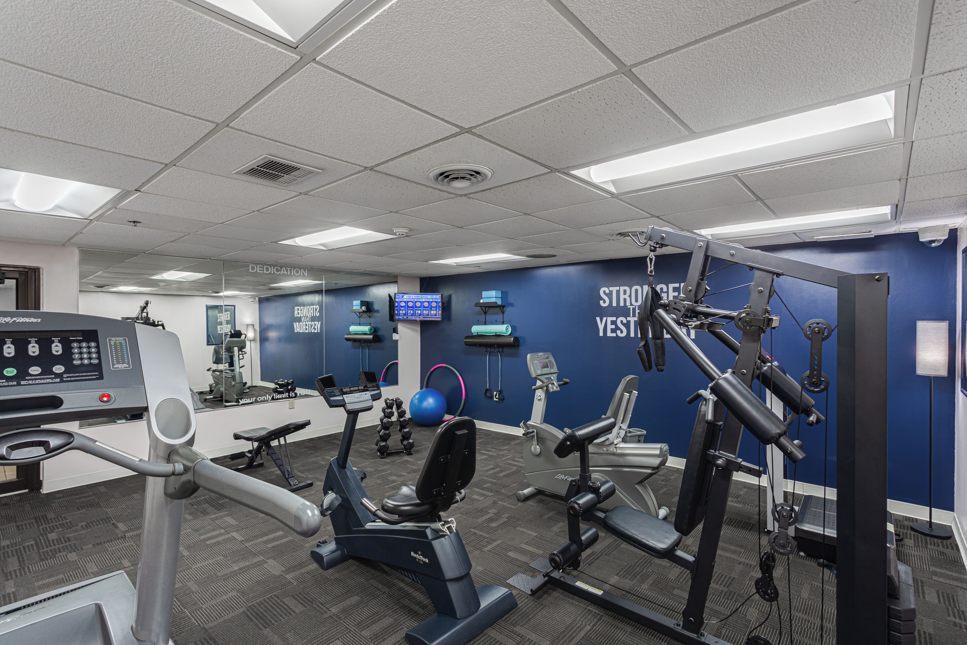 Un gimnasio con equipamiento de ejercicio, una pantalla digital y mensajes motivacionales en la pared.