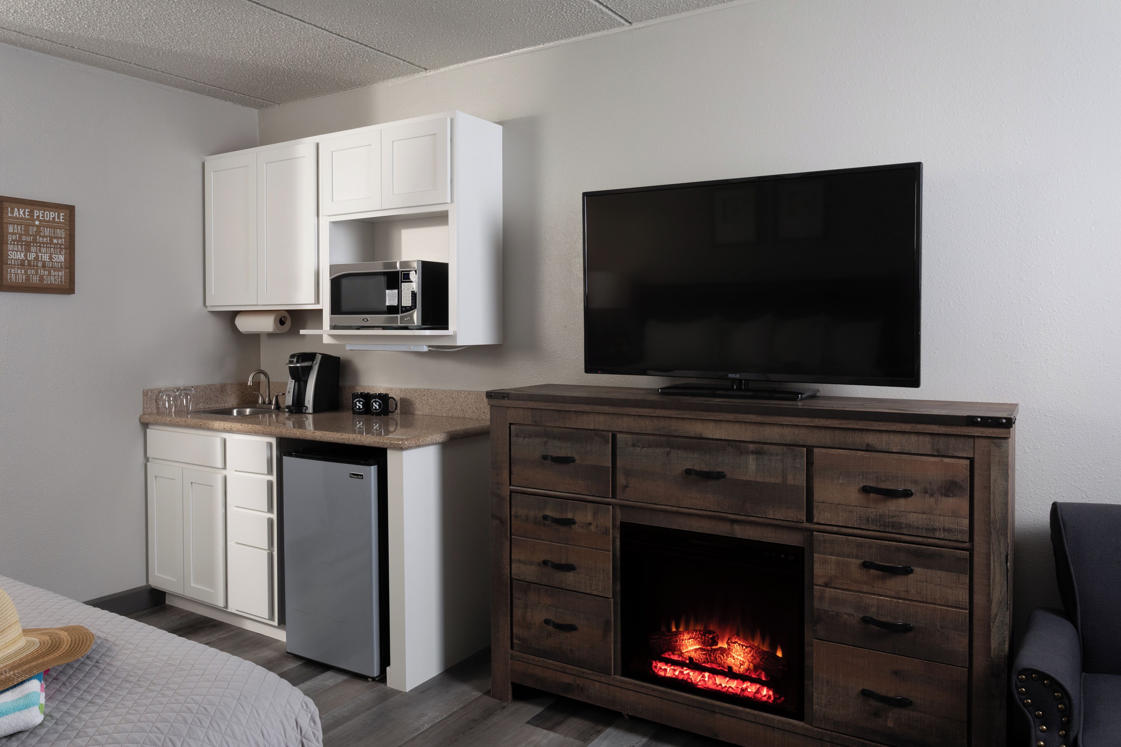 Cocina compacta con microondas, cafetera y televisor de pantalla plana sobre un mueble de madera con chimenea.