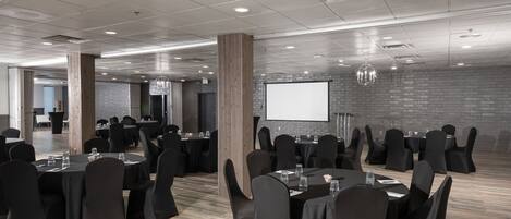A conference room with round tables, black chairs, and a projector screen.