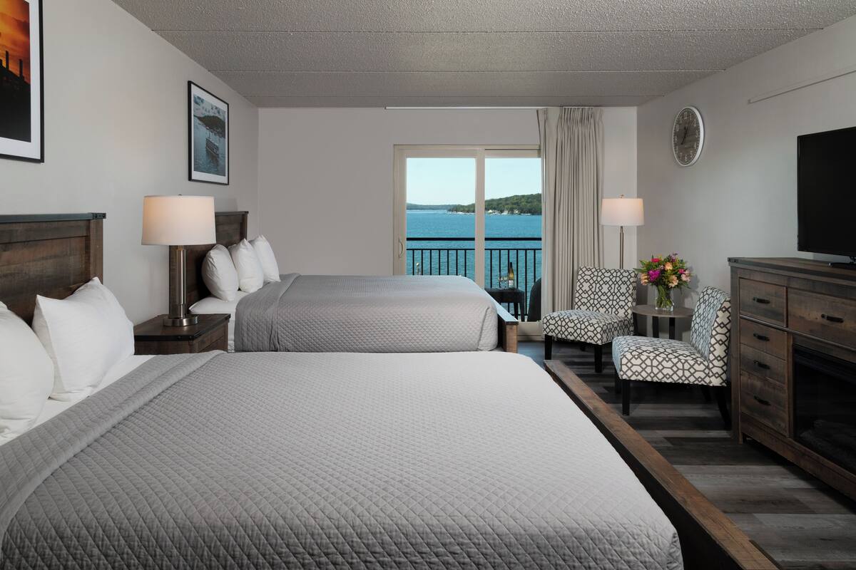Une chambre d’hôtel avec deux lits, une télévision, un bureau avec une chaise, une horloge et une vue sur la mer.