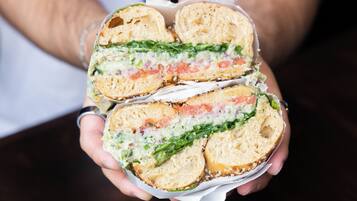 En person holder en sandwich med synlige lag af salat, tomat og en cremet dressing.