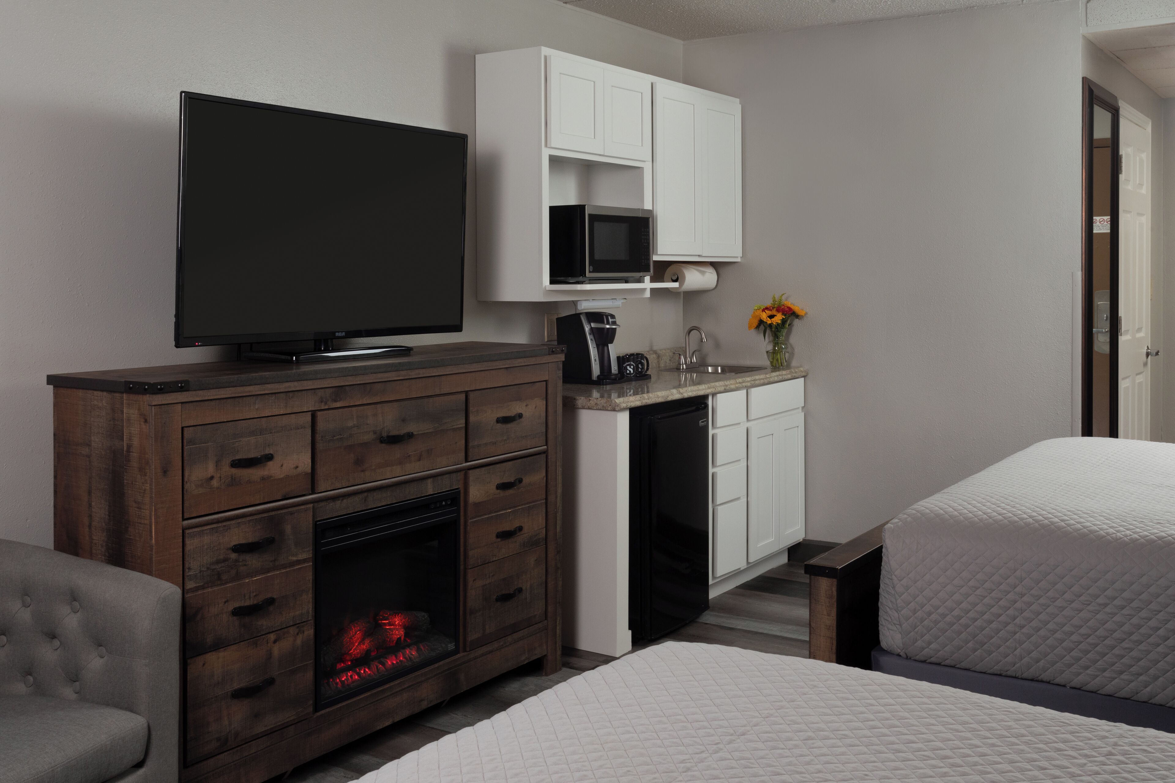 A hotel room with a TV, a fireplace, a kitchenette, and a bed.