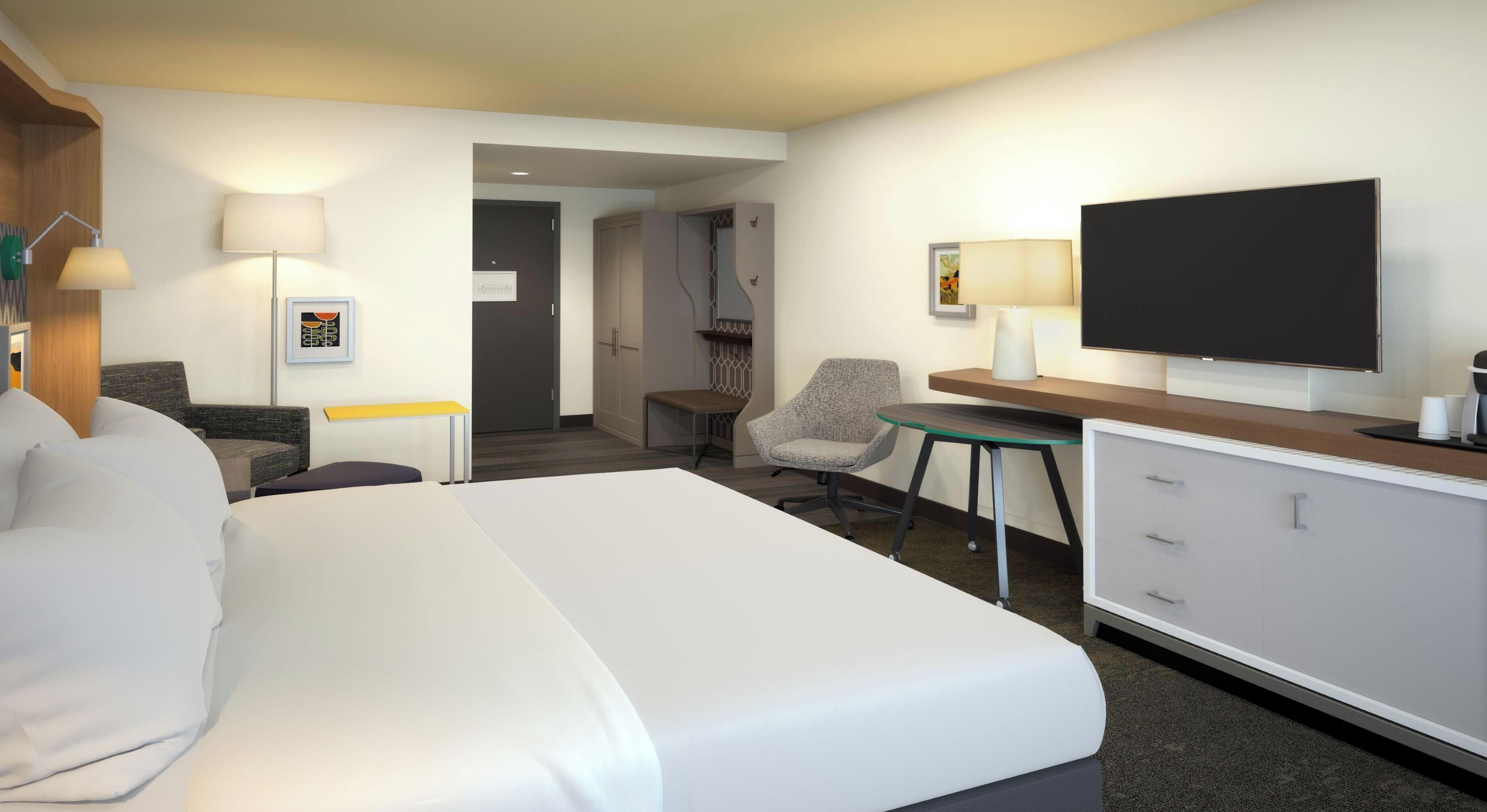 Une chambre d’hôtel avec un grand lit, un bureau, une chaise, une télévision et une porte donnant sur une salle de bain.