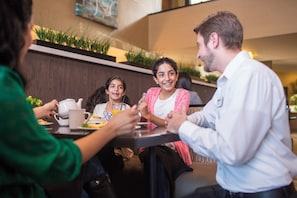 A group of people seated around a table in a modern indoor setting with a wooden accent wall and a plant display. - Holiday Inn Indianapolis Airport Area N by IHG (Indianapolis)