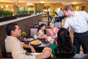 A group of people dining in a hotel restaurant with a waiter attending to them. - Holiday Inn Indianapolis Airport Area N by IHG (Indianapolis)
