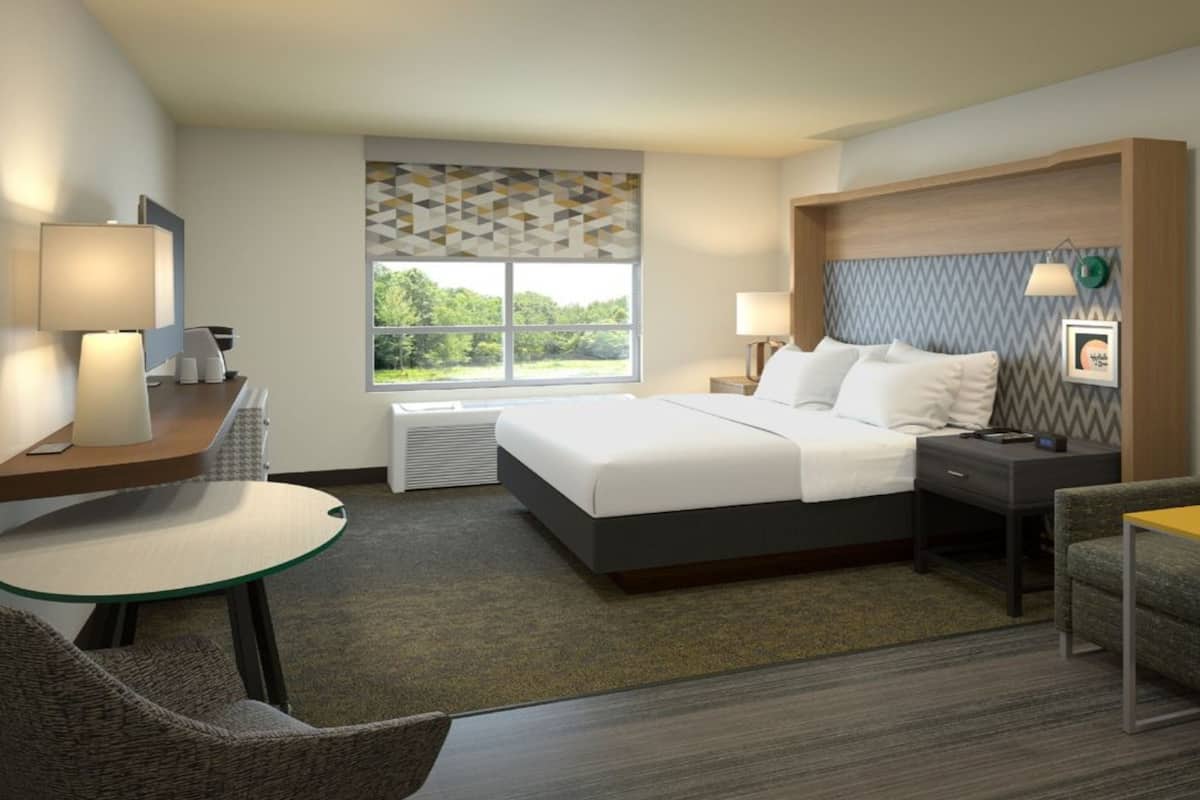 A hotel room with a bed, a desk with a chair, a sofa, a small table, and a window with a view of greenery.