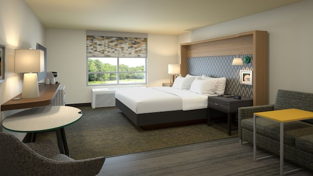 Une chambre d’hôtel comprenant un lit, un bureau avec une chaise, un canapé, une petite table et une fenêtre donnant sur un paysage verdoyant.