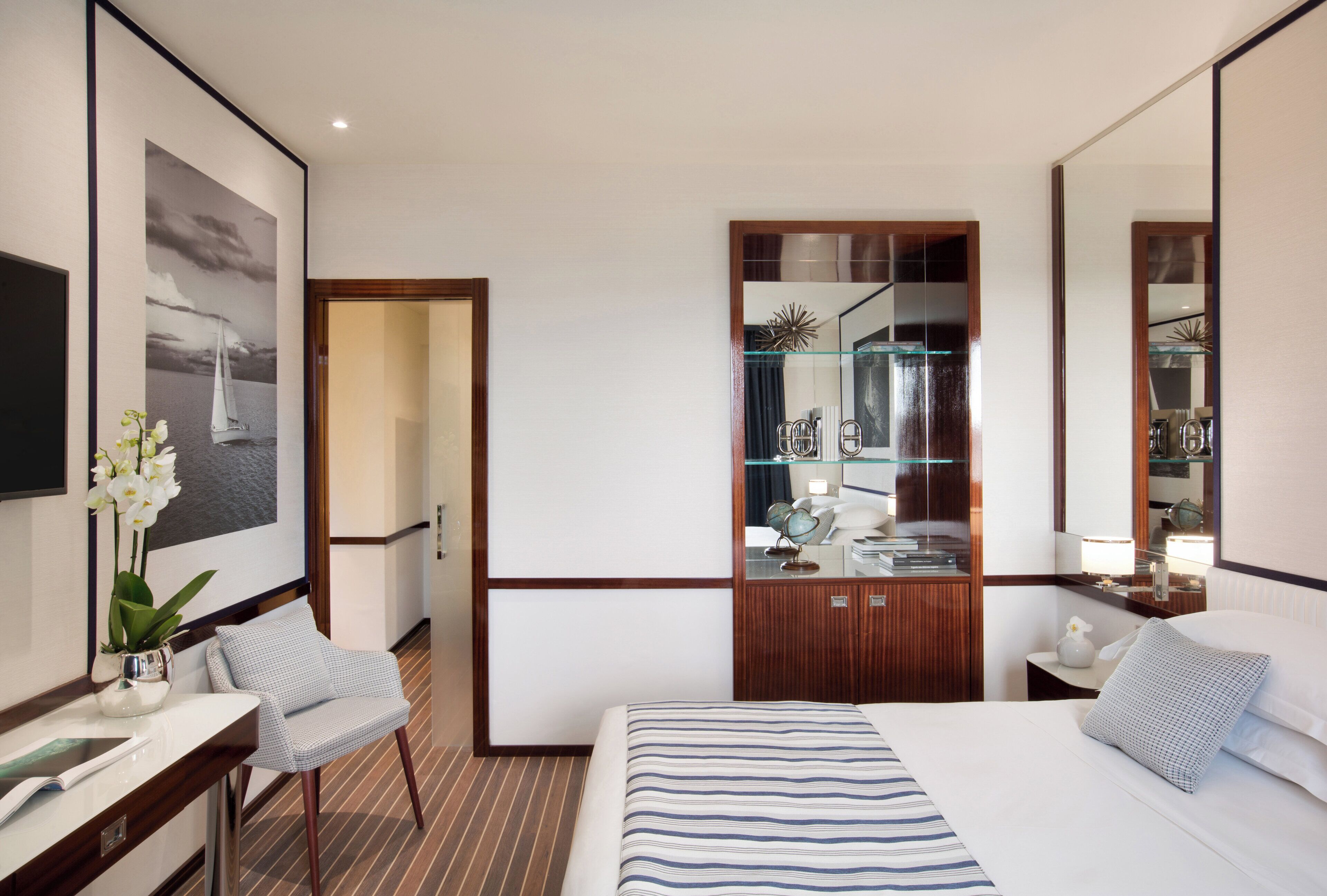 Een hotelkamer met een bed, een bureau met stoel, een grote spiegel en een garderobe met glazen deur.