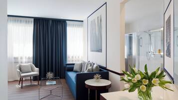 A modern hotel room with a sofa, armchair, and a glass shower enclosure.
