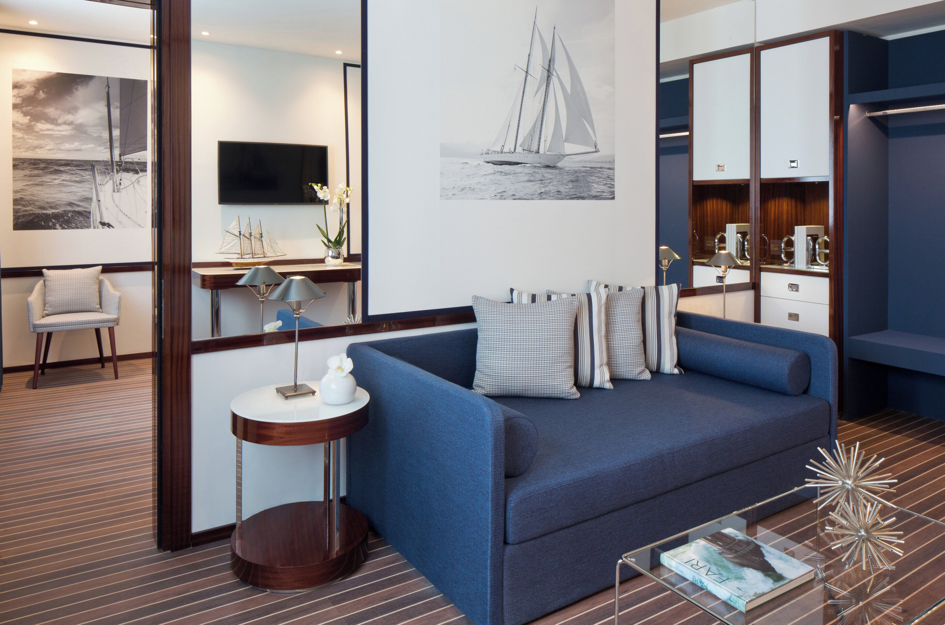 A modern hotel room with a blue sofa, a small round table, a flat-screen TV, and a large mirror.