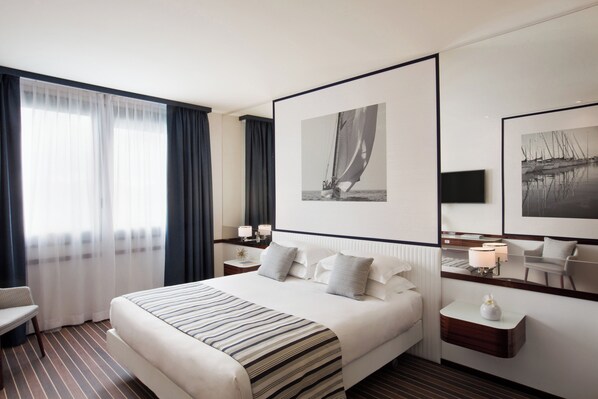 Een hotelkamer met een groot bed, een bureau, een stoel en twee ingelijste foto's aan de muur.