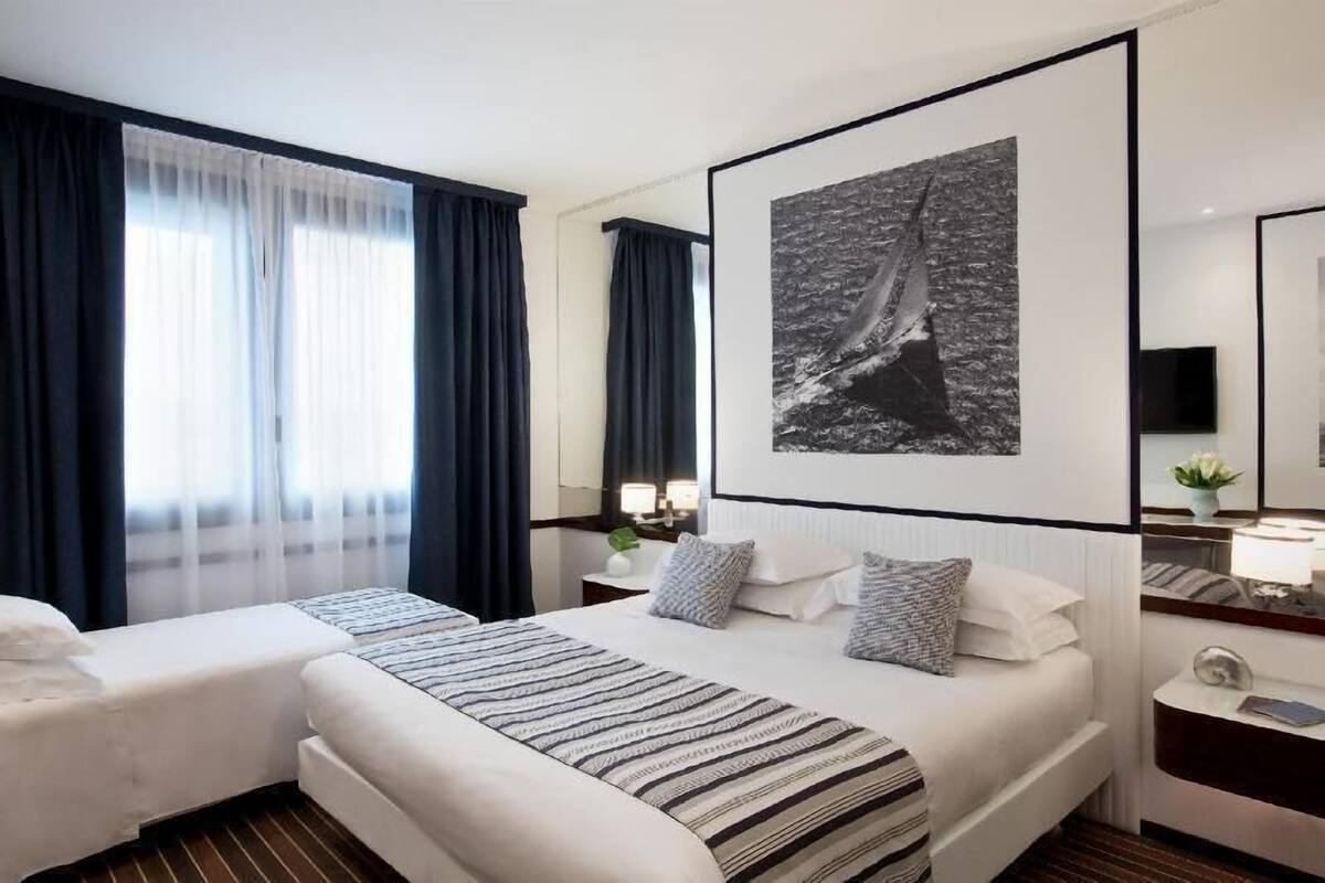 Une chambre d’hôtel avec un grand lit, un lit plus petit, une table de chevet avec une lampe, un miroir et un tableau encadré au mur.