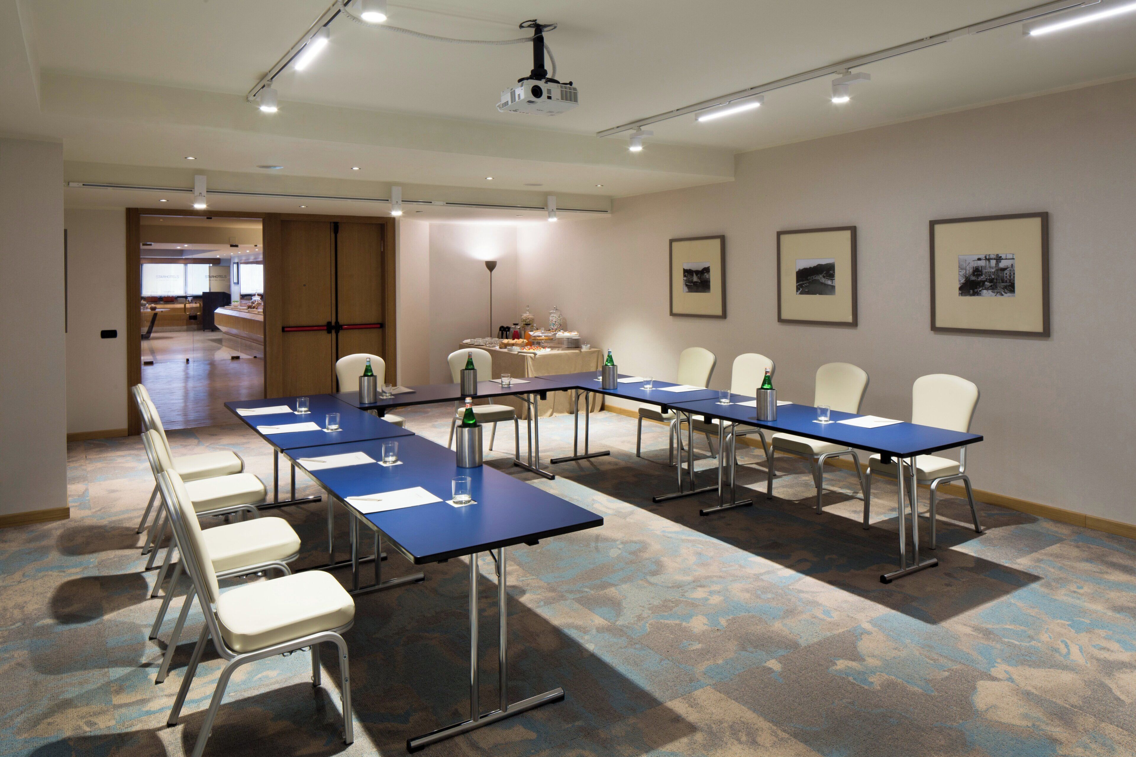 A conference room with long tables and chairs, a projector, and framed pictures on the wall.