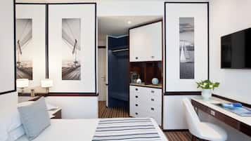 Ein Hotelzimmer mit Bett, Schreibtisch und Stuhl. An den Wänden hängen Bilder in Rahmen, auf dem Schreibtisch steht ein Globus und eine Pflanze.