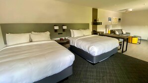 A hotel room with two beds, a desk, a chair, a lamp, and a trash can.