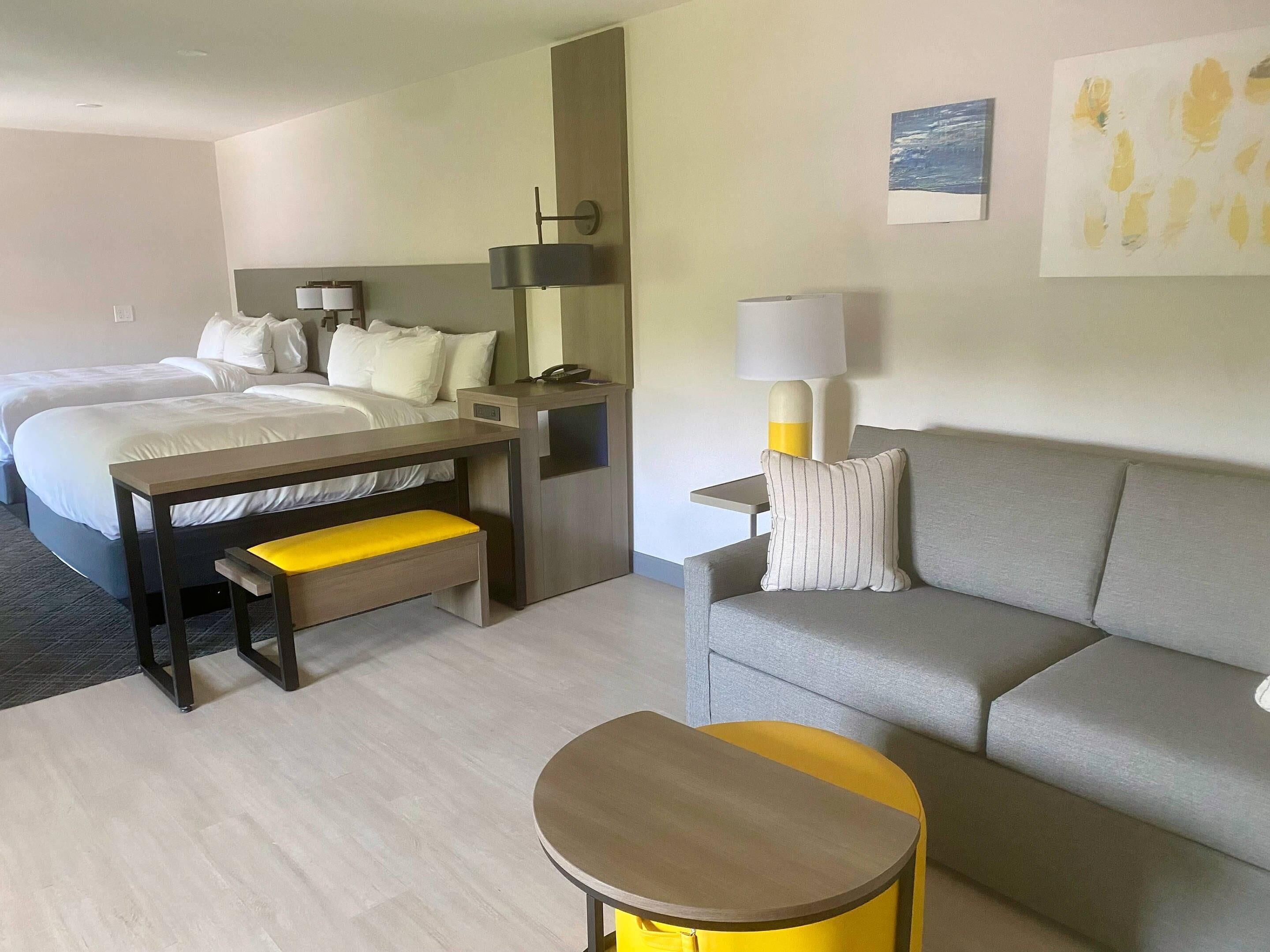A hotel room with two beds, a desk, a sofa, a small round table, and a lamp.