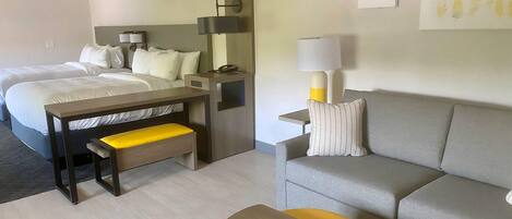 A hotel room with two beds, a desk, a sofa, a small round table, and a lamp.