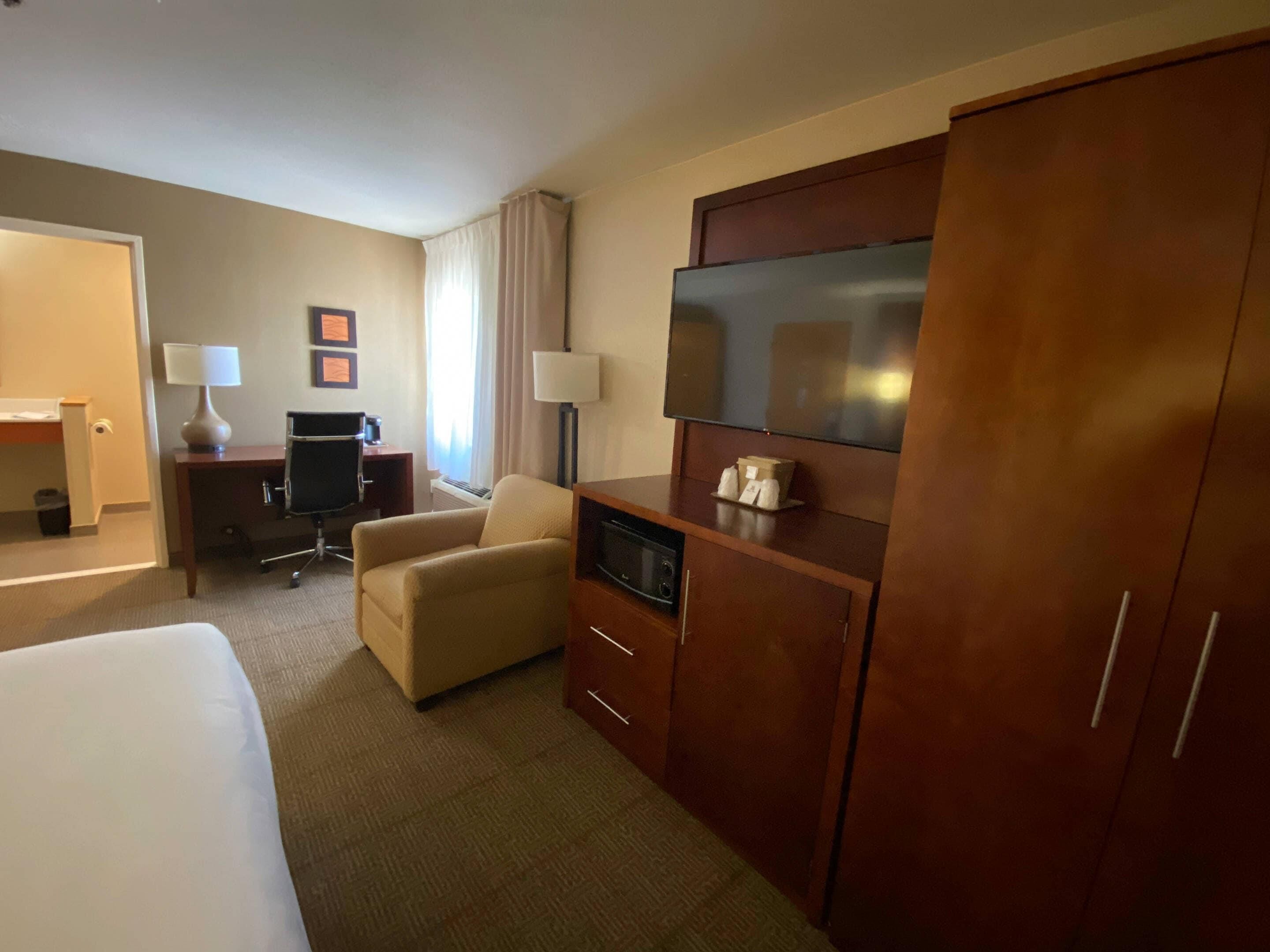 A hotel room with a bed, a desk, a chair, a TV, and a wardrobe.