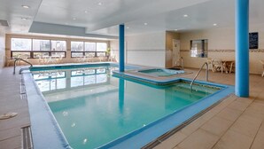 An indoor swimming pool with clear blue water, surrounded by white tiles and blue pillars.