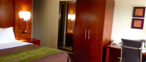 A hotel room with a bed, a desk, a chair, a wardrobe, and a mirror.
