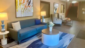 A modern hotel lobby with a blue sofa, a round coffee table, and abstract art on the walls.