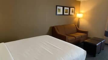 A hotel room with a large bed, a brown sofa, a small table, and a floor lamp.