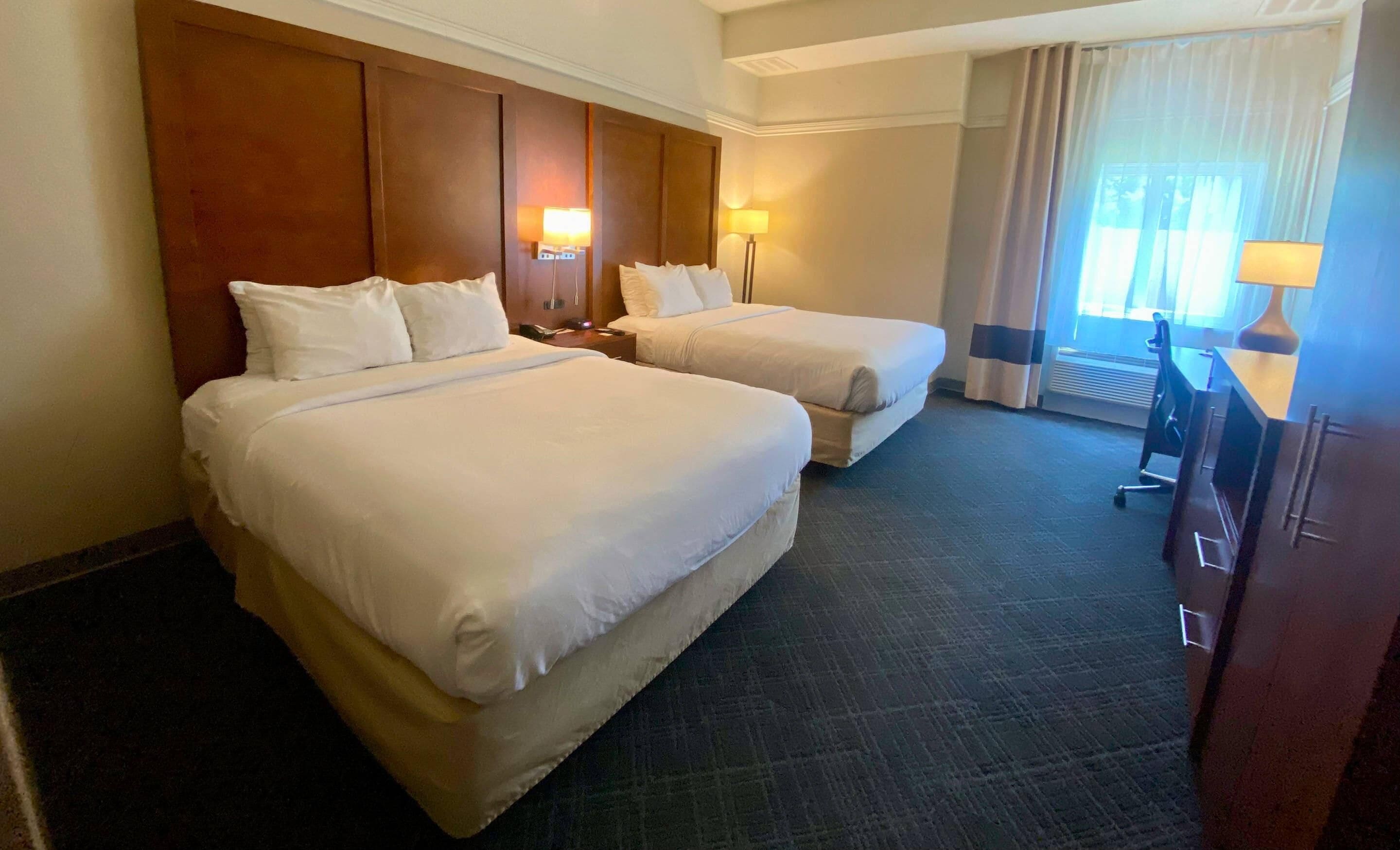 A hotel room with two beds, a desk, and a chair.