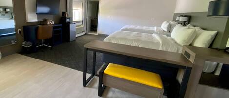 A modern hotel room with a bed, a desk, a chair, a TV, and a bathroom visible through an open door.